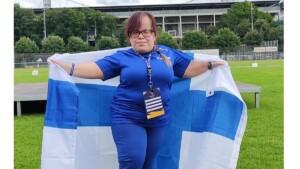 Nainen sinisessä urheiluasussa pitää Suomen lippua takanaan.