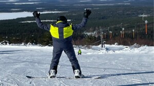 Henkilö laskettelurinteen huipulla. Hänet on kuvattu selästä päin ja hän käyttää lumilautaa.