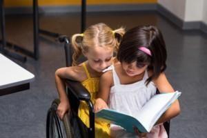 Kaksi lasta istuu sylikkäin pyörätuolissa ja lukevat kirjaa