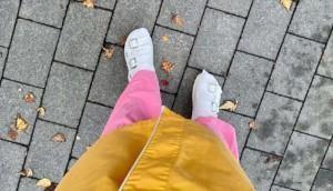 Valkoiset sandaalijalat yläpuolelta otetussa kuvassa, jossa näkyvät myös pinkit pyjamalahkeet ja keltainen sairaala-aamutakki. Taustana harmaa laattakiveys.