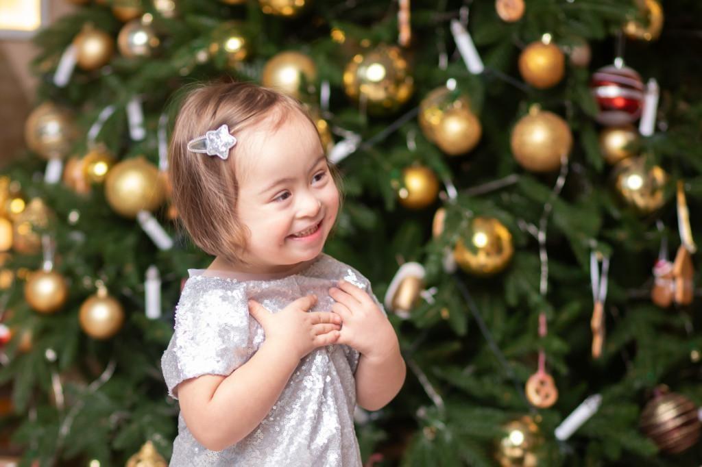 hymyilevä lapsi joulukuusen edessä pitää käsiä ristissä rinnan päällä