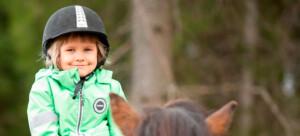 Tyttö vihreässä takissa hevosen selässä.