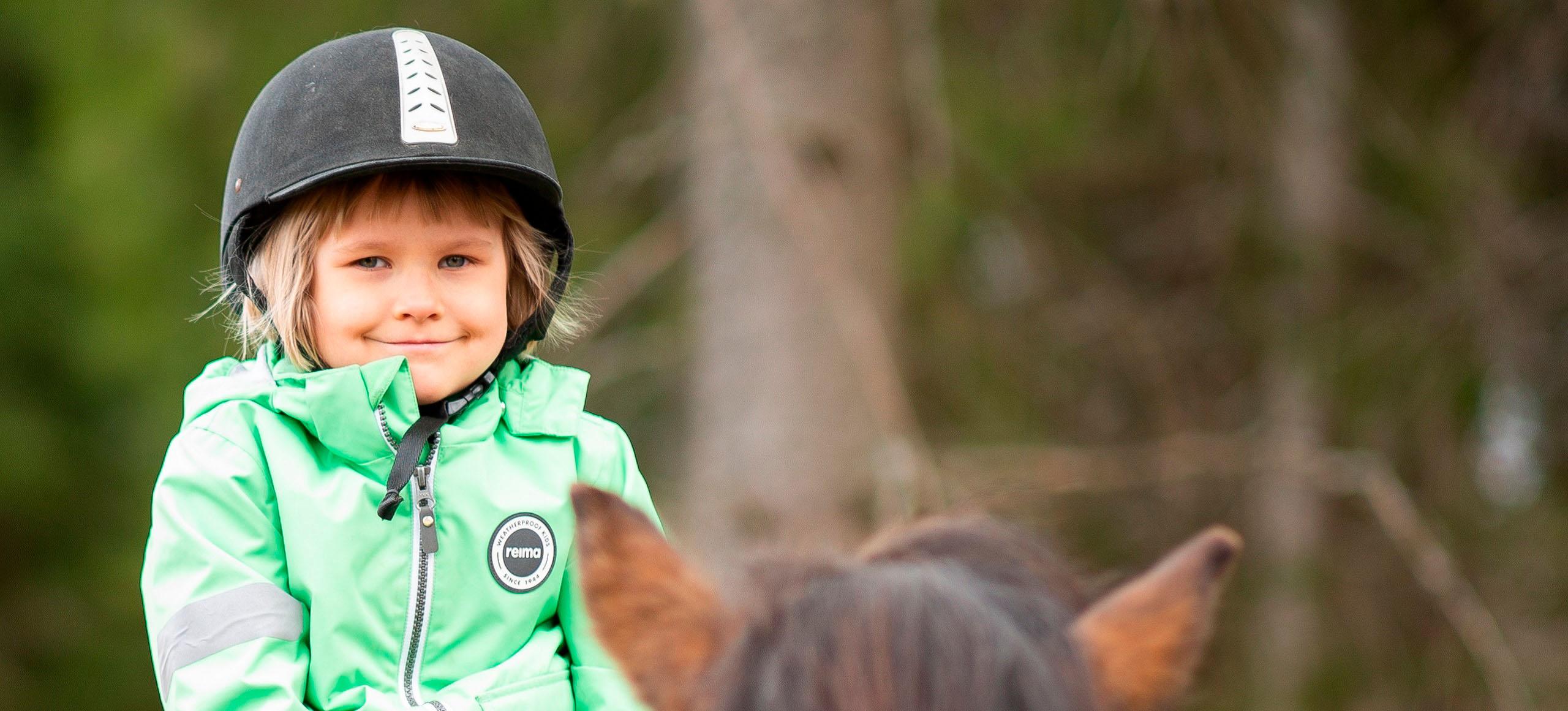 Tyttö vihreässä takissa hevosen selässä.