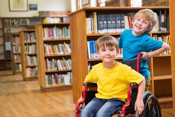 Kaksi poikaa kirjastossa. Toinen heistä istuu pyörätuolissa.